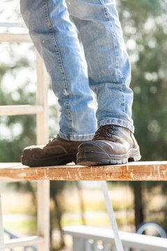 Tradie feet and boots on plank for painting high up
