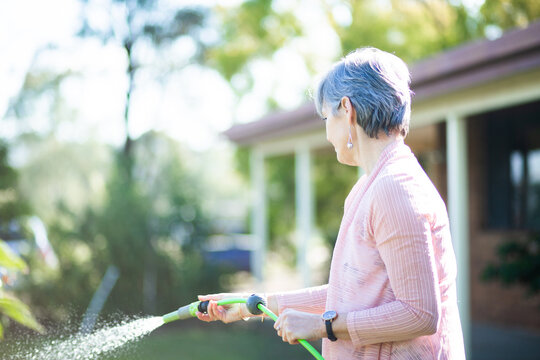 Middle aged woman watering her garden beside her house