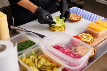 The cook in the kitchen is cooking a cheeseburger and putting a lettuce leaf.