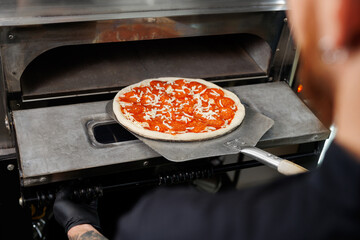 Pizzaiolo takes the finished pizza out of the electric oven. Ppizzaiolo holds a pizza on a spatula.