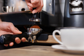 Fototapeta na wymiar Macro shot of barista pressing ground coffee using tamper. Close-up view on hands.