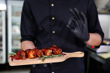 The cook holds a board with barbecue ribs and fresh rosemary in his hands.