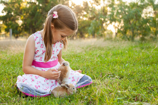Young girl playing outside with two little brown rabbits