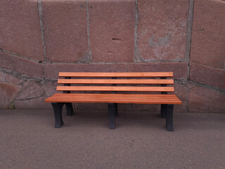 Empty wooden bench in the sidewalk against red granite wall
