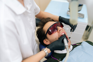 Female dentist using modern diode dental laser for periodontal care, top view. Male patient wearing...