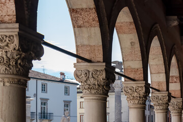 Columns of Loggia del Lionello with scenic view of Venetian style clock tower Torre dell'Orologio on main square Piazza della Liberta in historic old town Udine, Friuli Venezia Giulia, Italy, Europe - obrazy, fototapety, plakaty