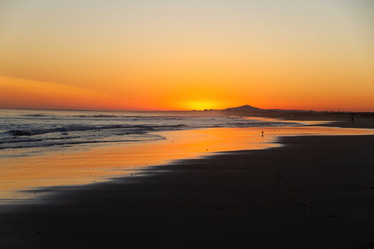 Sunset on beach at low tide with reflections of the orange sky in the water, The Algarve, Portugal