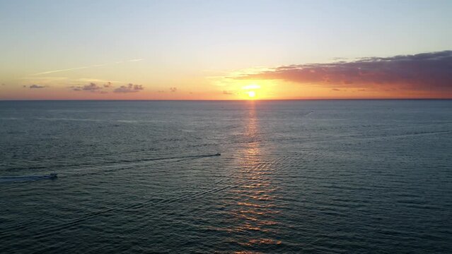 Beautiful following drone shot of sunrise over the Atlantic Ocean with 2 boats in the distance heading out to sea.
