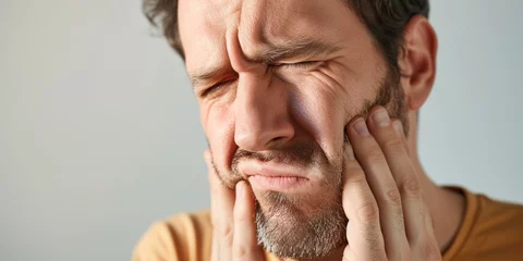 Fotobehang Male pressing sore cheek on studio background. Adult man suffers acute toothache, periodontal disease, cavities or jaw pain almost crying with pain ache © Valeriia
