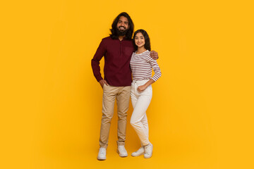 Cheerful young indian couple posing on yellow background, full length © Prostock-studio