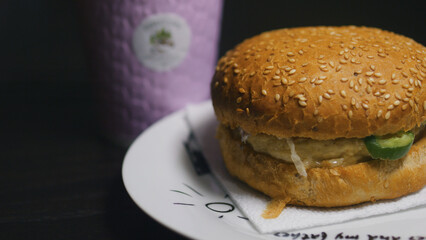 Cheeseburger on a plate with a purple paper cup on the background. Close up.