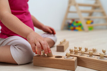 A 2.5 year old child sorts shapes of different sizes. Wood childrens game by Montessori system. Wooden knobbed cylinders for preschool and kidergarten playing.