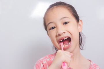 Close-up shots of adorable Asian kid who is brushing her teeth in the morning. Her front view shows an adorable face with joy and a clean smile for routine dental caring in bright bathroom.