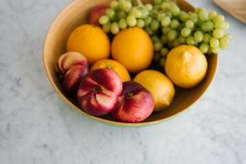 Fresh fruit, peaches, grapes and oranges in a plate on the marble table in the kitchen. Healthy and wholesome food