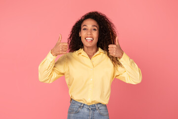 Smiling black woman giving two thumbs up on pink background