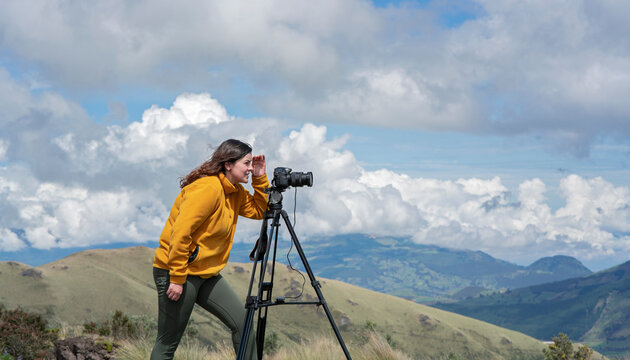 Beautiful young Latin American woman with her camera and tripod taking photos of landscapes on the top of a mountain