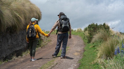 Young Latin American couple with backpacks walking holding hands on a trail in the middle of the wasteland on a mountain