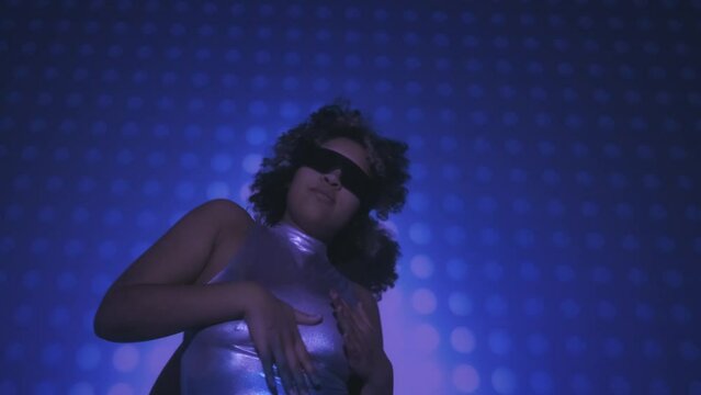 Low angle view shot footage of young Black woman wearing disco style outfit and eyeglasses dancing in projector light