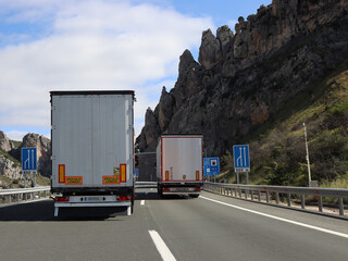 Behind overtaking lorries on steep two-lane motorway through mountains blocking other road users - 729342583