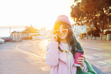 Young smiling hipster woman with color hair holding reusable coffee cup wearing pink coat, knitted...
