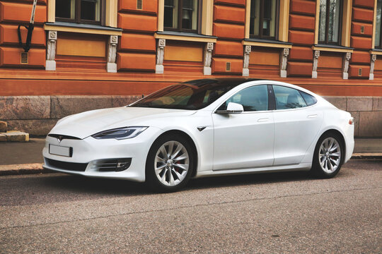 Beautiful white Tesla Model S fully electric car parked by city street outside old building.