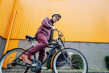 Bottom view Young stylish man in helmet riding on cruiser city Bicycle near orange Wall. Student on...