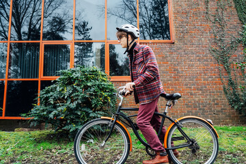 Young stylish man in helmet riding on cruiser city Bicycle on urban sidewalk to the office. Student...