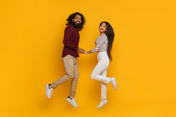 Fototapeta na wymiar Positive carefree indian man and woman holding hands, jumping