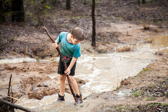 Boy playing in muddy creek with brown flowing water