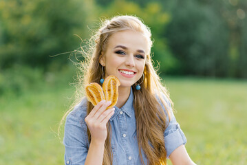 Smiling young woman with a pastry in her hand lies on a blanket at a summer picnic