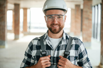 Positive smiling construction worker in uniform in empty unfinished room