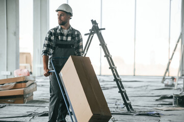 Walking and transporting the paper box. Repairman in uniform is in the unfinished building