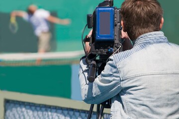 a cameraman films a tennis player playing on a bright sunny day