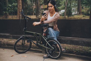 Happy young Asian woman while riding a bicycle in a city park. She smiled using the bicycle of...