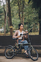 Happy young Asian woman while riding a bicycle in a city park. She smiled using the bicycle of transportation. Environmentally friendly concept.