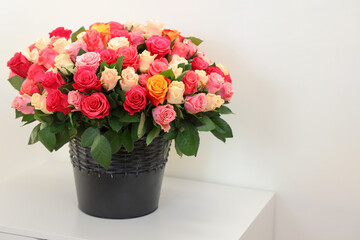 Bouquet of beautiful roses on white bedside table, space for text