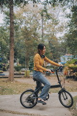 Obraz premium Happy young Asian woman while riding a bicycle in a city park. She smiled using the bicycle of transportation. Environmentally friendly concept.