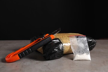 Smuggling, drug trafficking. Packages with narcotics and utility knife on grey table against black...