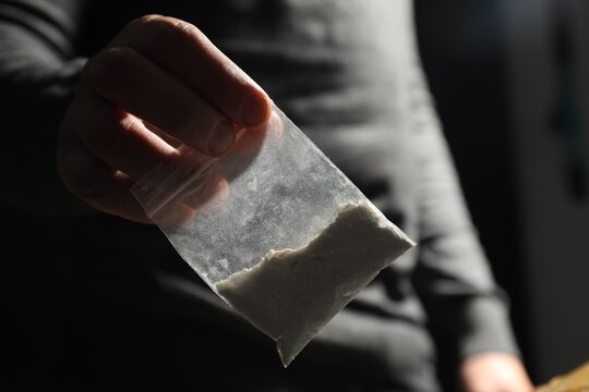 Drug addiction. Man giving plastic bag with cocaine on dark background, closeup