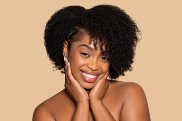 Joyful african american woman with hands on cheeks and curly hair, beige backdrop