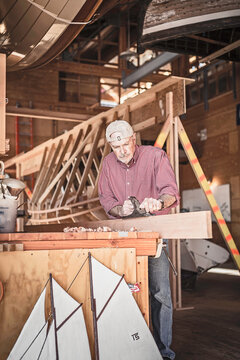 Senior man building and working on a wooden boat in a workshop. Port Townsend, Washington, USA