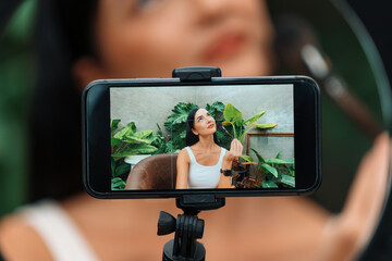 Rear view woman make natural beauty and cosmetic tutorial on green plant garden video content display on phone screen. Beauty blogger showing how to beauty care to social medial audience. Blithe
