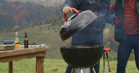 Close up shot of two men together cooking meat on grill. Active leisure on beautiful hill. Family...