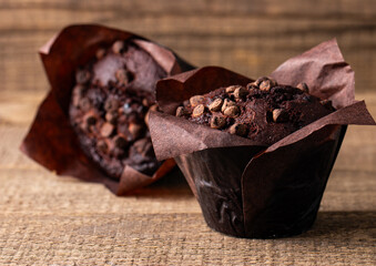 Chocolate dark muffin with chocolate chips and drops on a wooden table  - obrazy, fototapety, plakaty