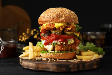 Delicious burger with crispy chicken patty and french fries on black wooden table