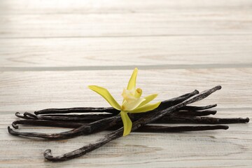Vanilla pods and beautiful flower on white wooden table, closeup. Space for text