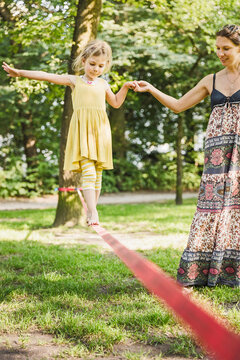 Mother helping daughter over a slack line.