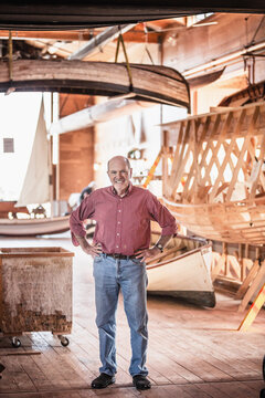Portrait of older man in front of the wooden boat he is building.