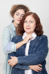 An elderly mother and an adult daughter are looking at the camera. The daughter-in-law gently hugs her mother-in-law.