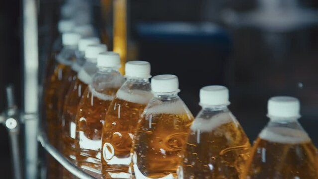 Side closeup of capped plastic bottles of carbonated drink moving along conveyor belt and hand of unrecognizable worker taking one bottle out of production line at beverage factory